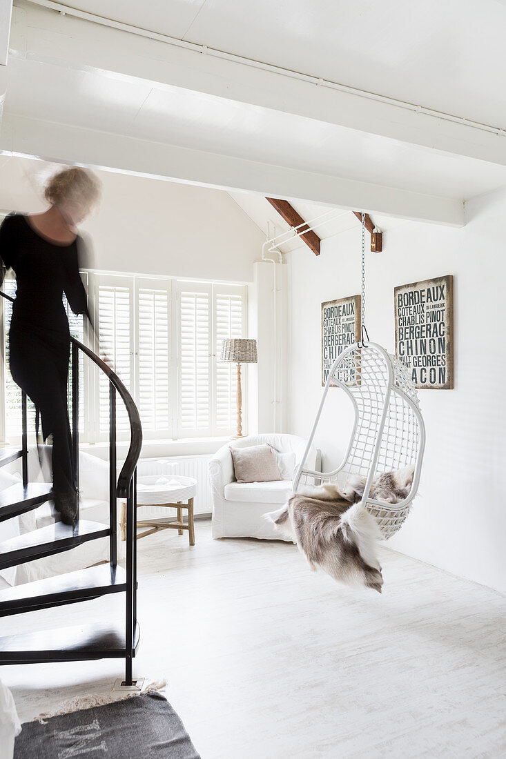 Frau auf Wendeltreppe zum weißen Wohnzimmer mit Hängesessel