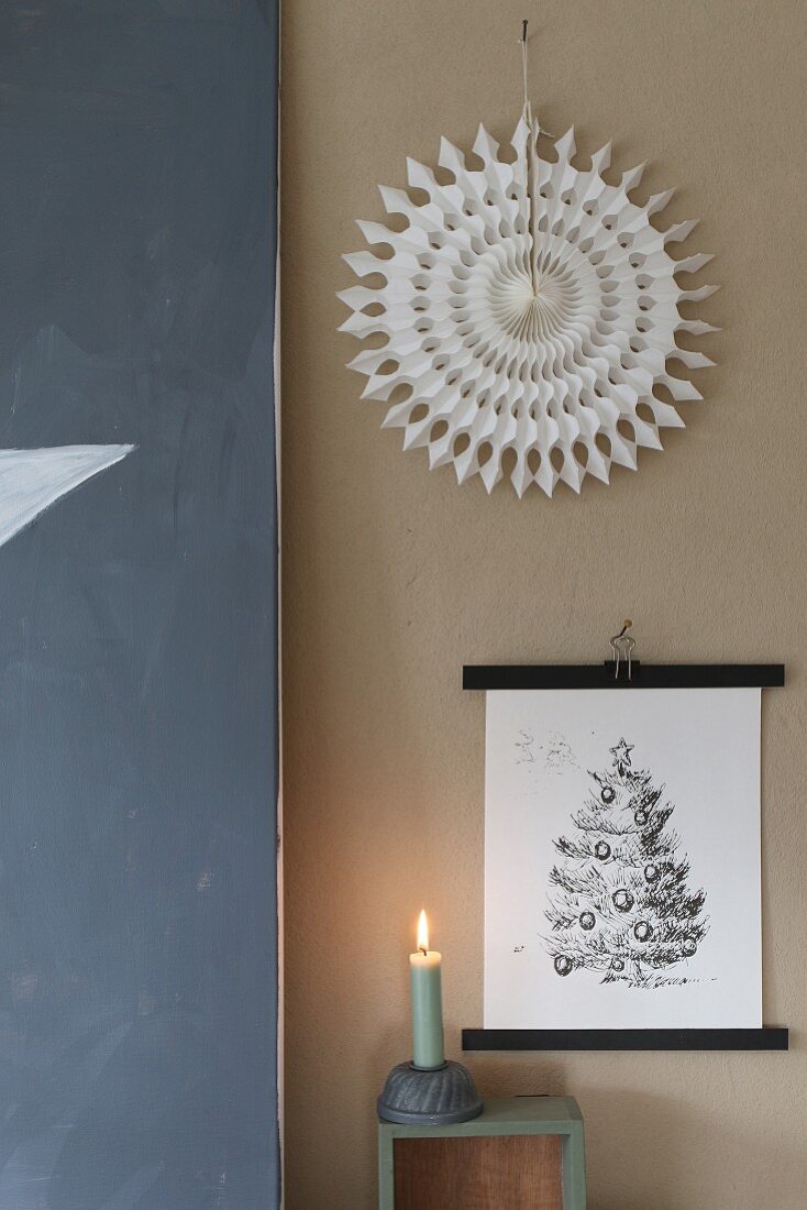 Festive arrangement of picture, paper sunburst and lit candle against wall