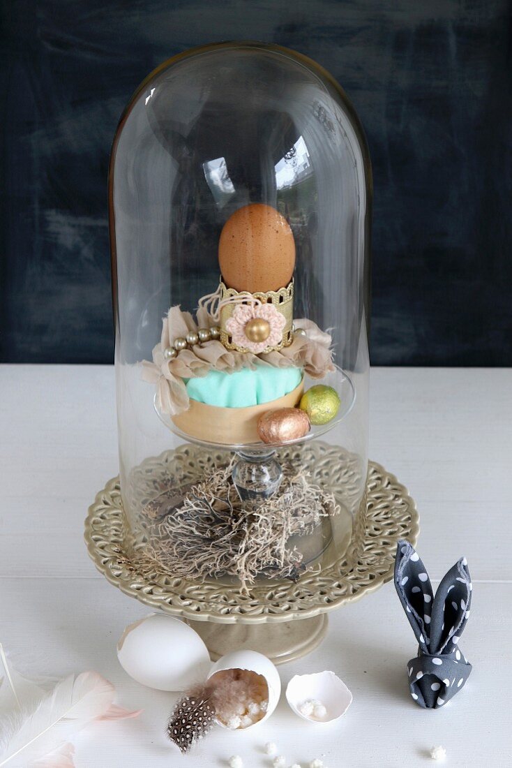 Easter arrangement under glass cover, egg shells, feathers and napkin bunny