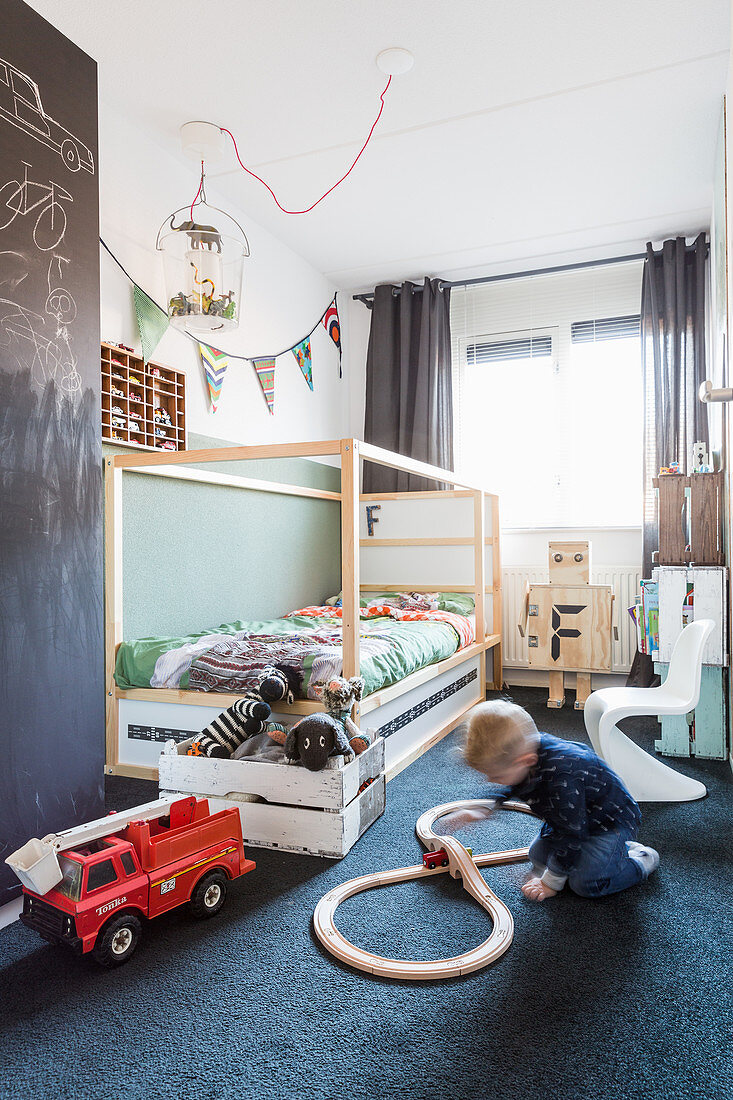 Junge spielt vor dem Bett auf dem Boden im Kinderzimmer