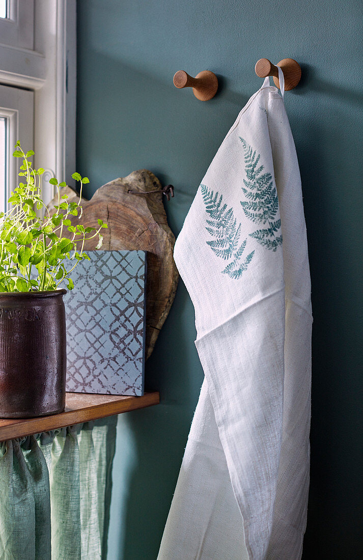 Tea towel printed with fern leaves hung on green wall