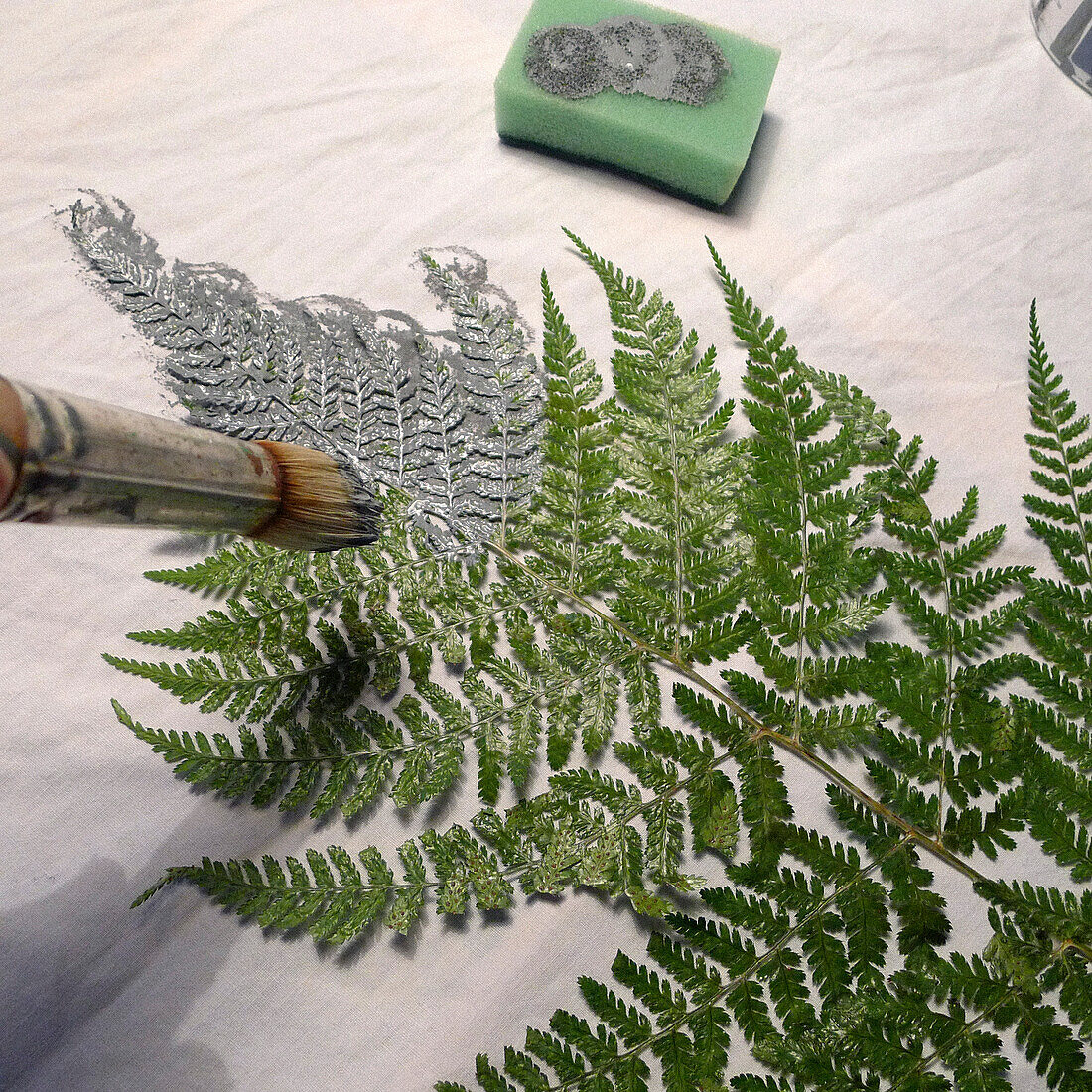 Dabbing grey paint onto a fern leaf using a paintbrush