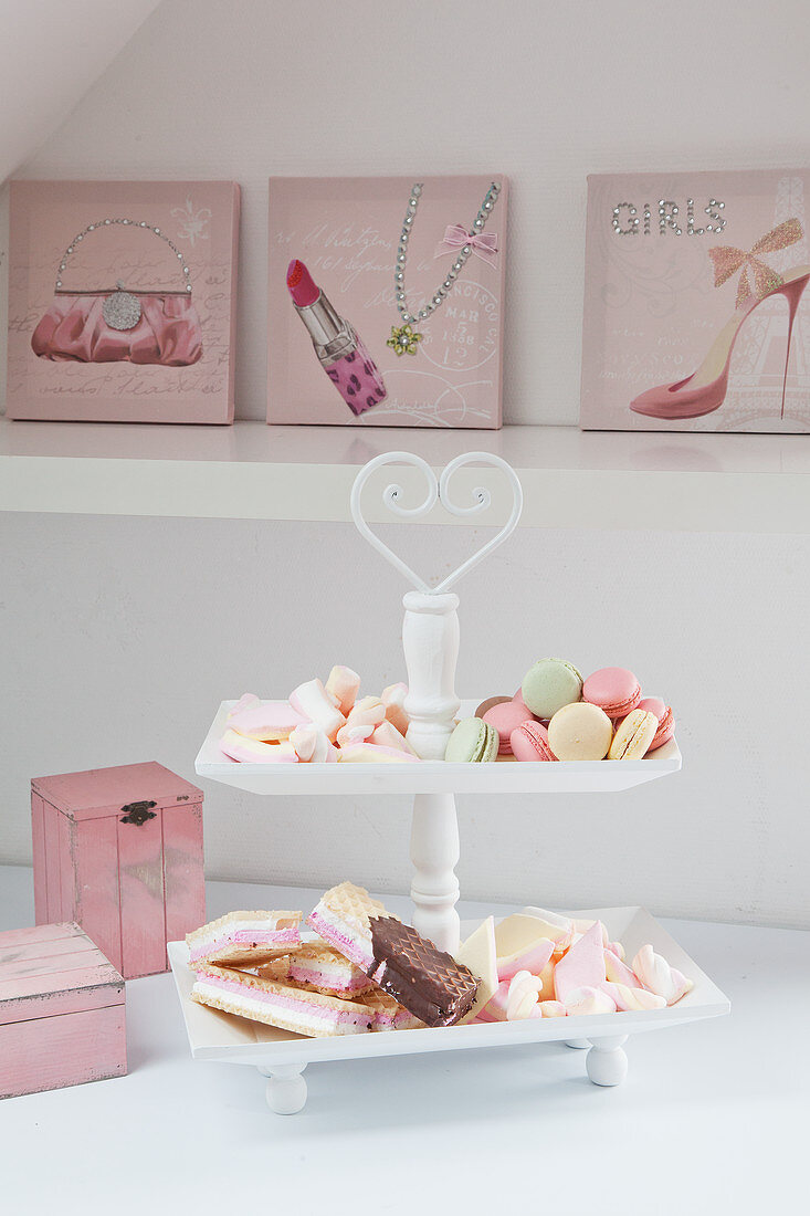 Pastel-coloured pastries on cake stand in front of feminine pictures