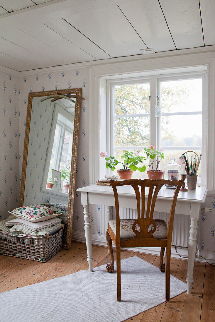 Stuhl im Jugendstil an einem weißen Tisch vorm Fenster, Korb mit Kissen vorm Bodenspiegel