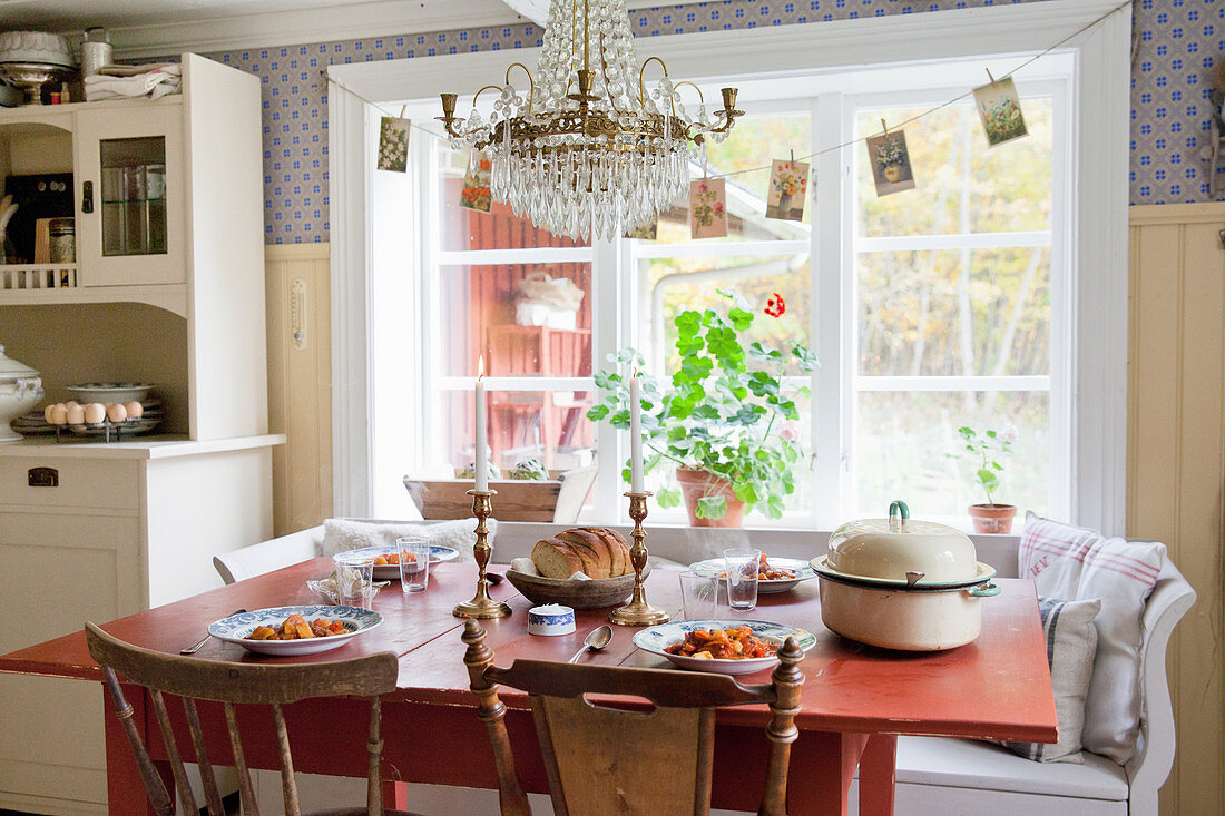 Gedeckter roter Tisch vor dem Fenster in skandinavischer Landhausküche