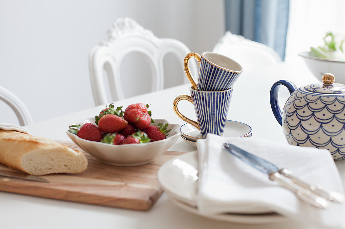 Gedeckter Tisch mit Erdbeeren, Baguette und blau gemustertem Geschirr