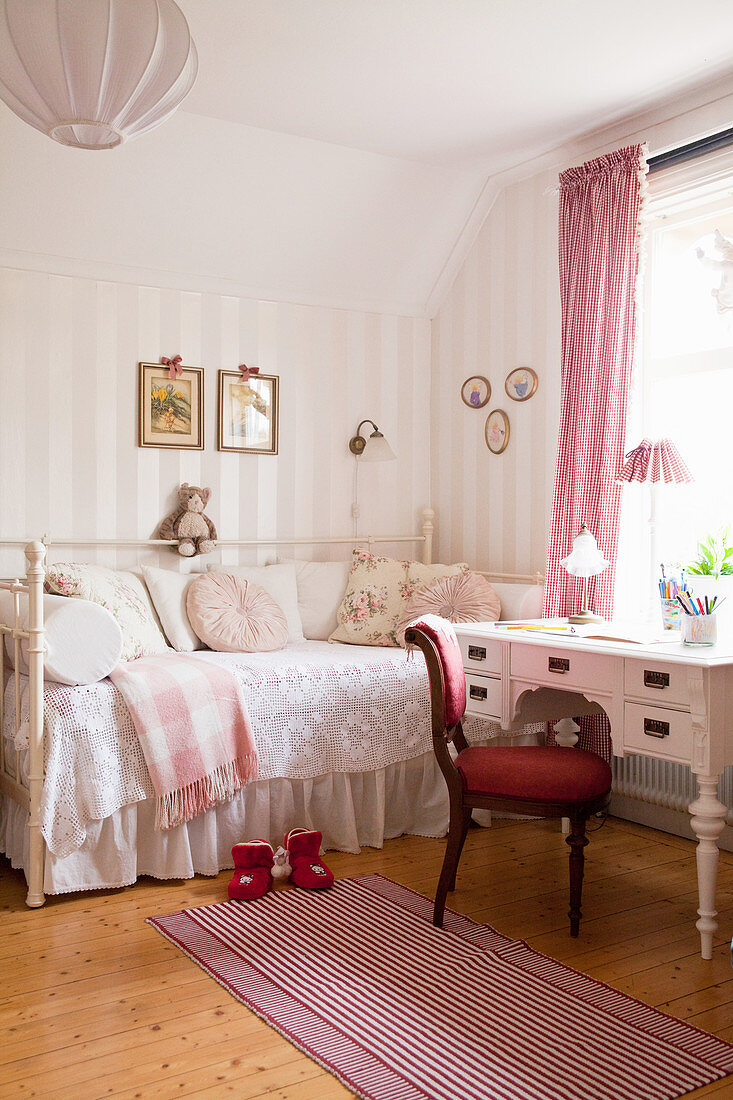 Roter Polsterstuhl und antiker Schreibtisch vorm romantischen Bett im Kinderzimmer