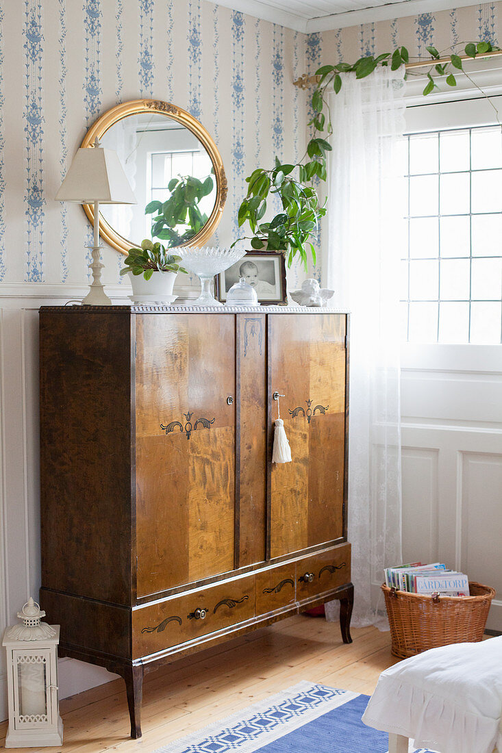 Antique wooden cabinet against blue-and-white wallpaper