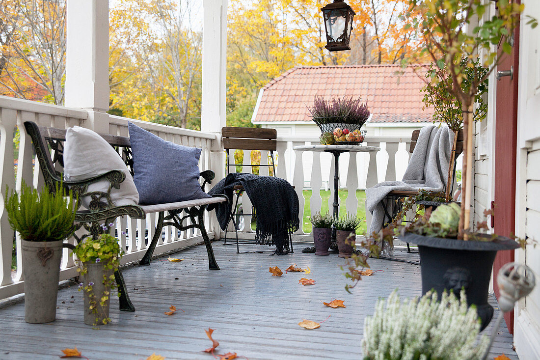 Chairs at bistro table and iron bench on veranda with autumn decorations