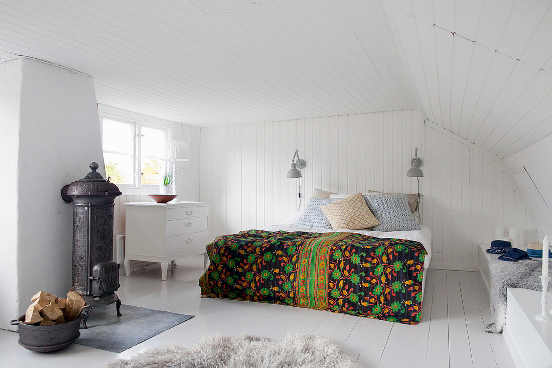 Colourful bedspread on bed in bedroom with cast-iron stove