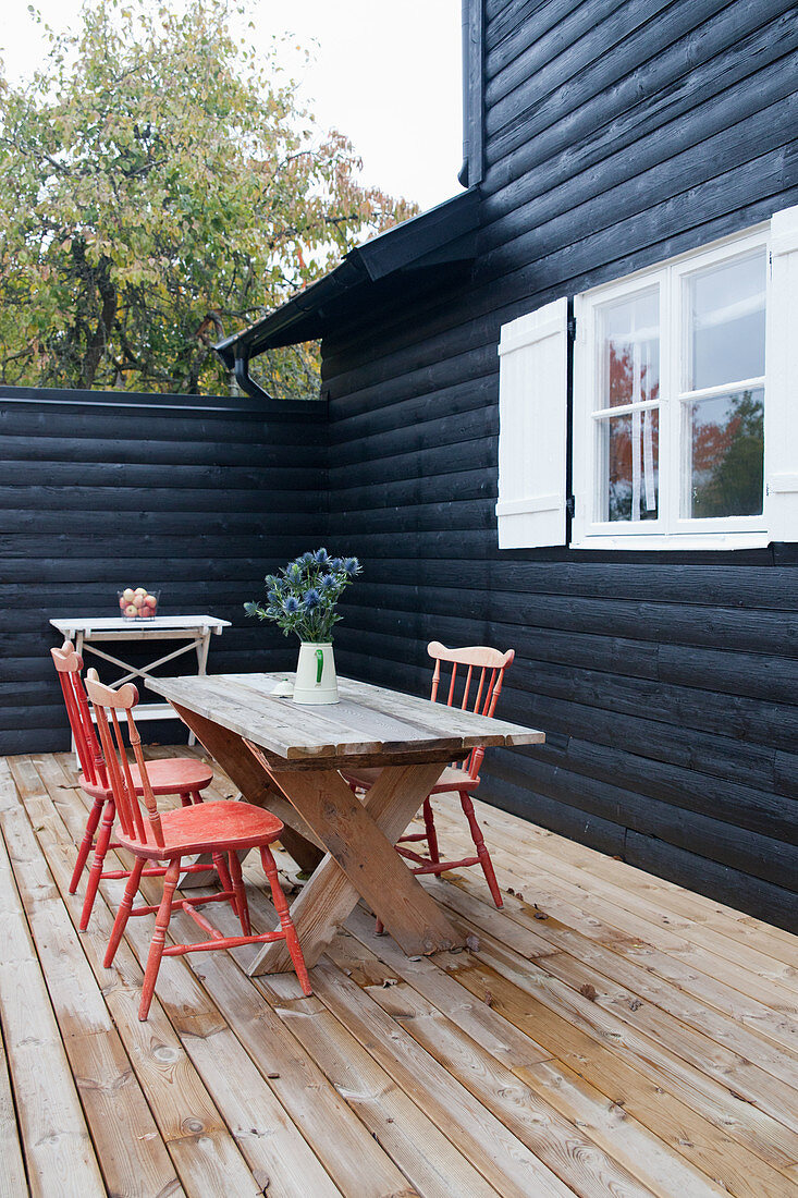 Rote Sprossenstühle am Holztisch auf der Terrasse am schwarzen Holzhaus