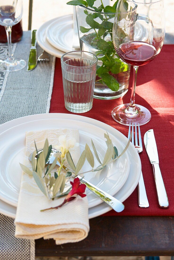 Place settings with olive sprig and flower on red tablecloth