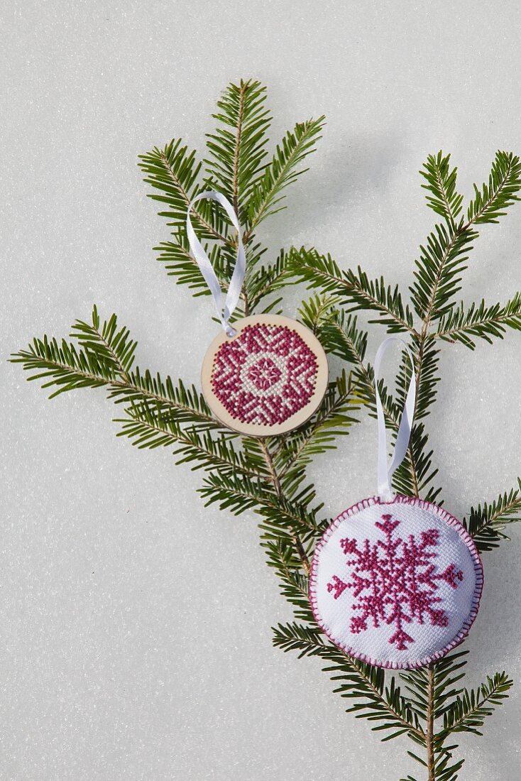 Two hand-made embroidered snowflake decorations on green fir branch