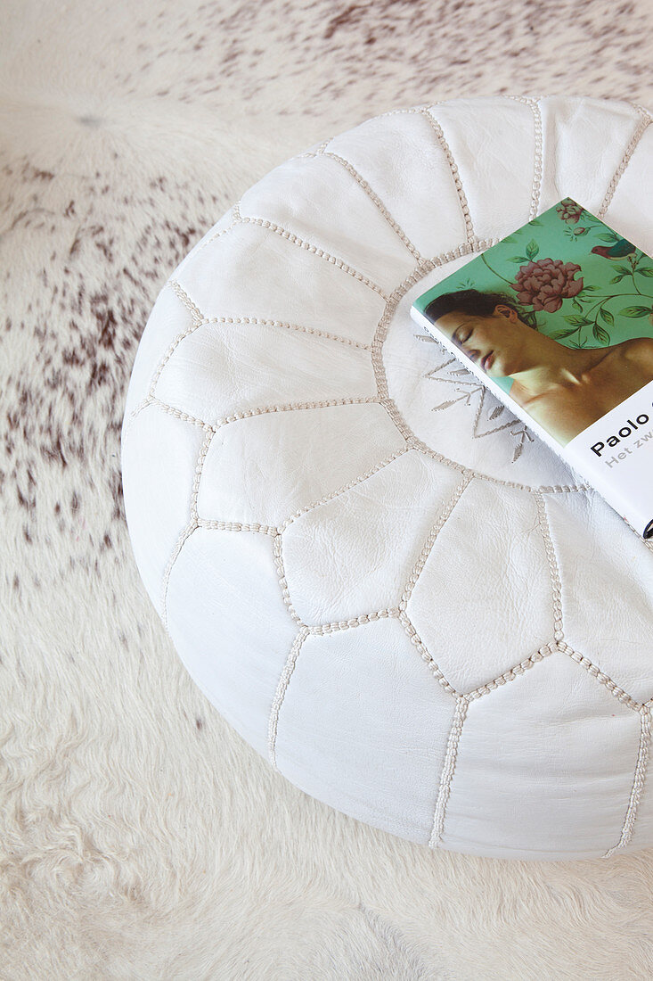 Book on white leather pouffe on white cowhide rug