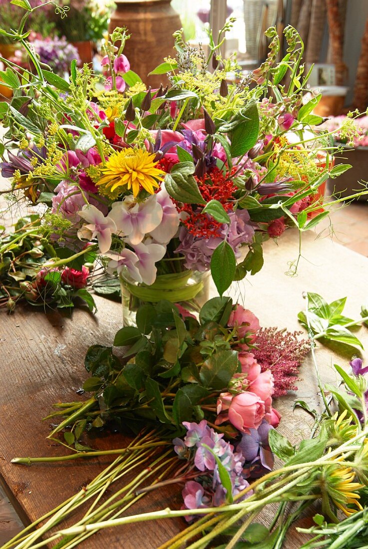 Bunter Sommerblumenstrauß in Glasvase neben Schnittblumen auf Holztisch