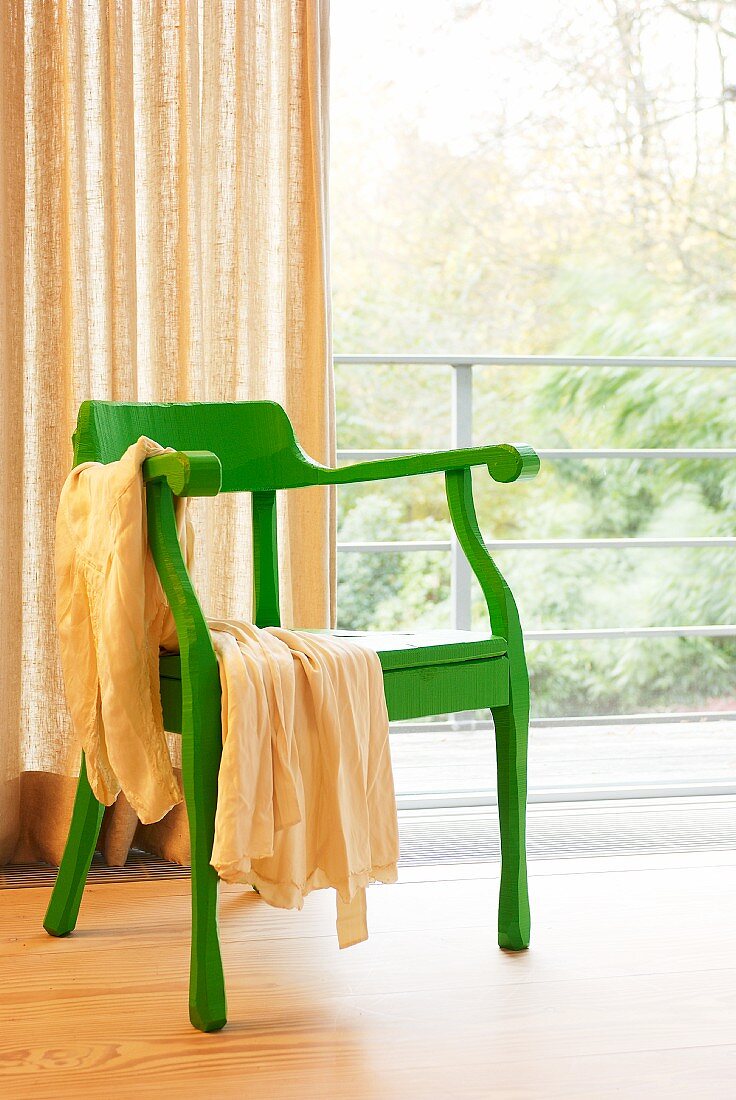 Green retro armchair in front of glass wall with curtain