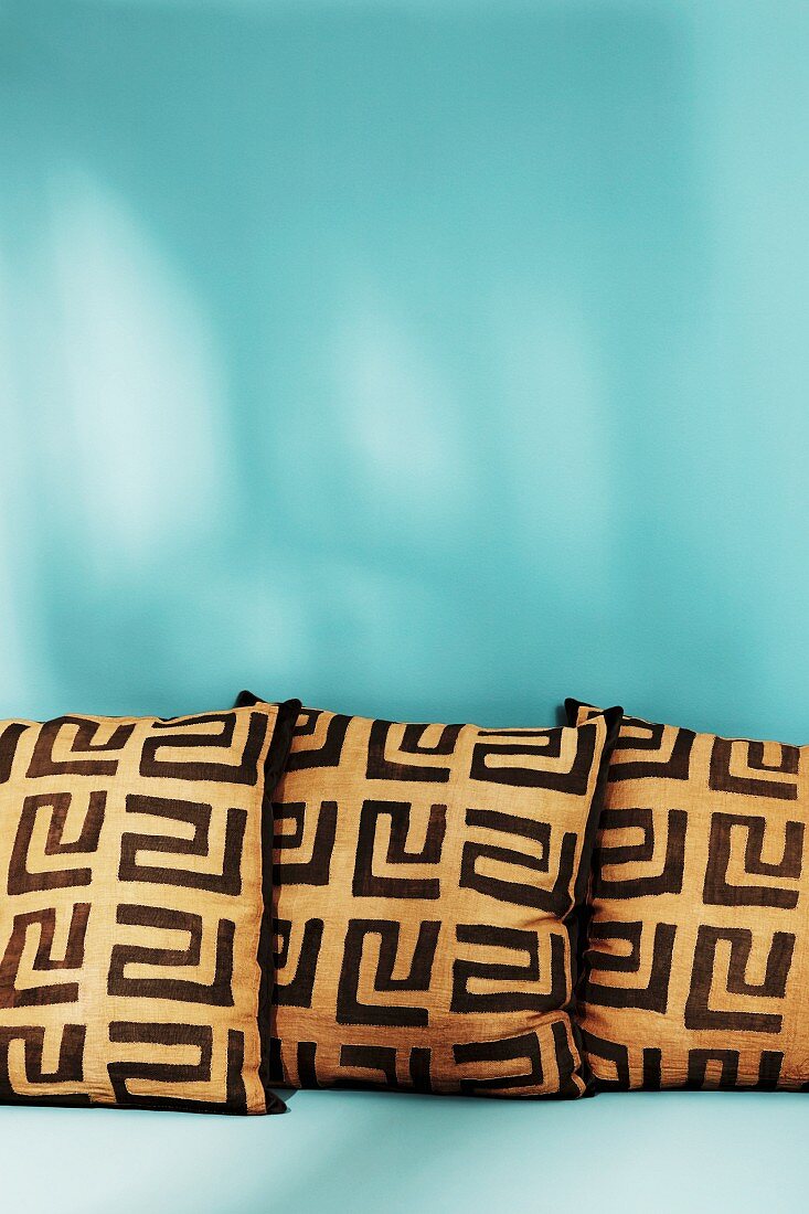 Three cushions with graphic patterns against turquoise background