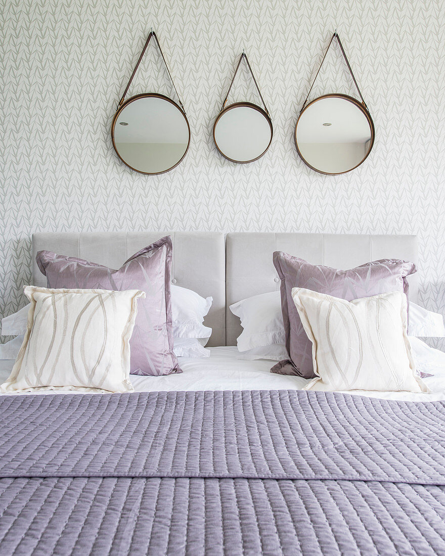 Drei runde Spiegel hängen über dem Bett mit lilafarbenen Kissen