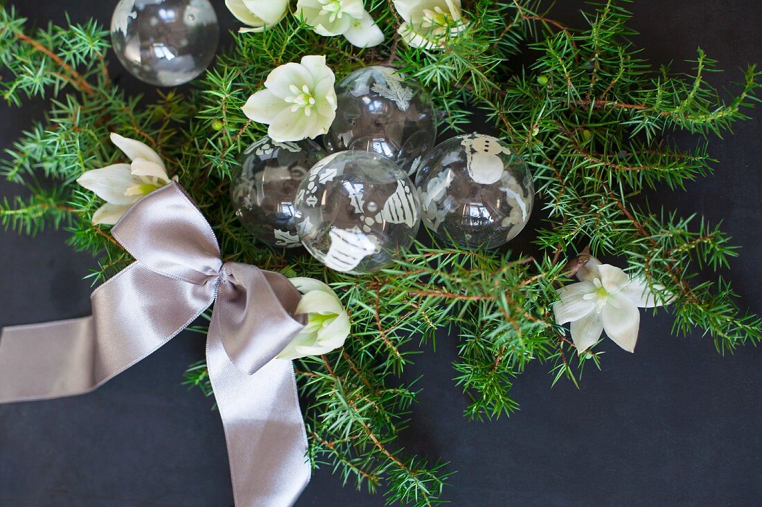Glass Christmas-tree baubles, green conifer branches, hellebore flowers and satin ribbon