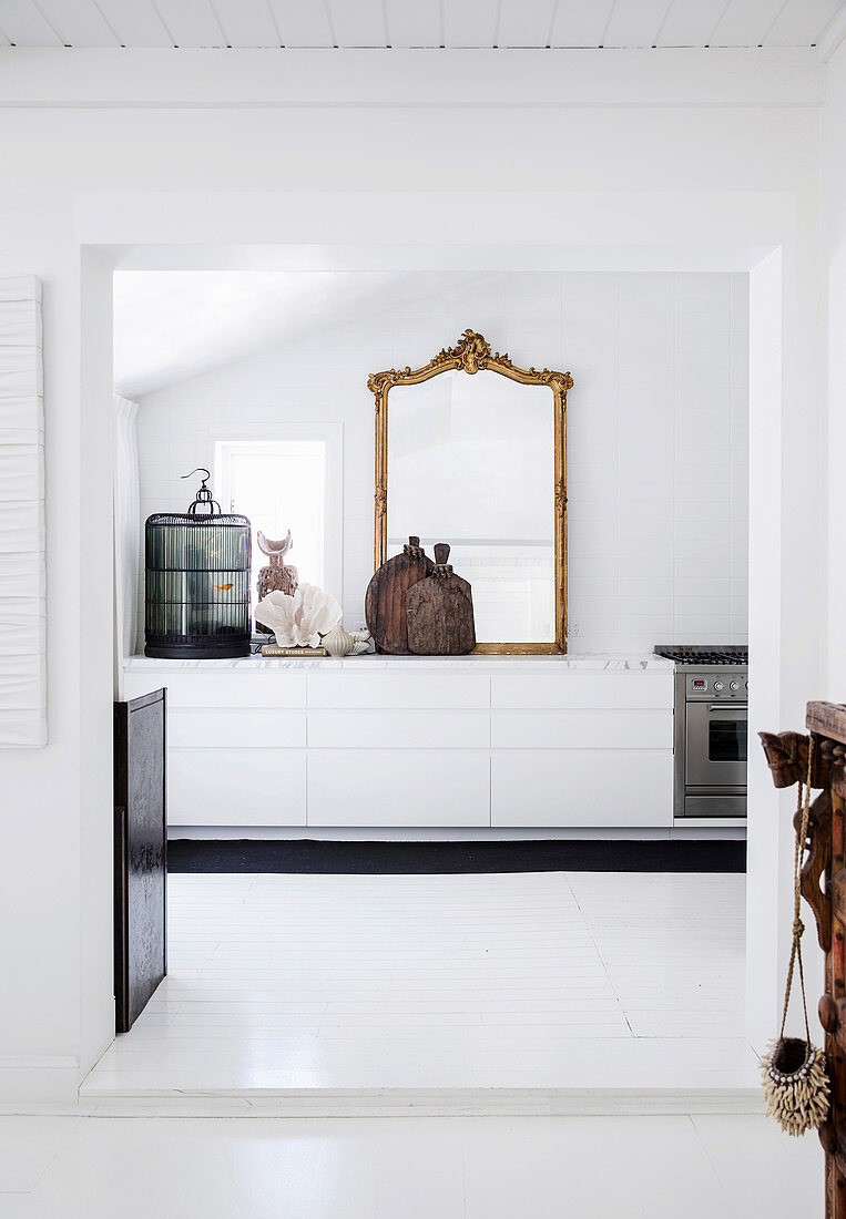 Blick auf weiße Küchenzeile mit antikem Goldrahmenspiegel und Käfig