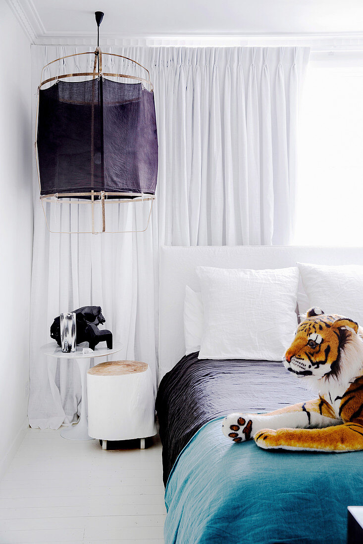 Schlafzimmer mit Stofftier, Nachttisch und Hängelampe vor weißem Vorhang