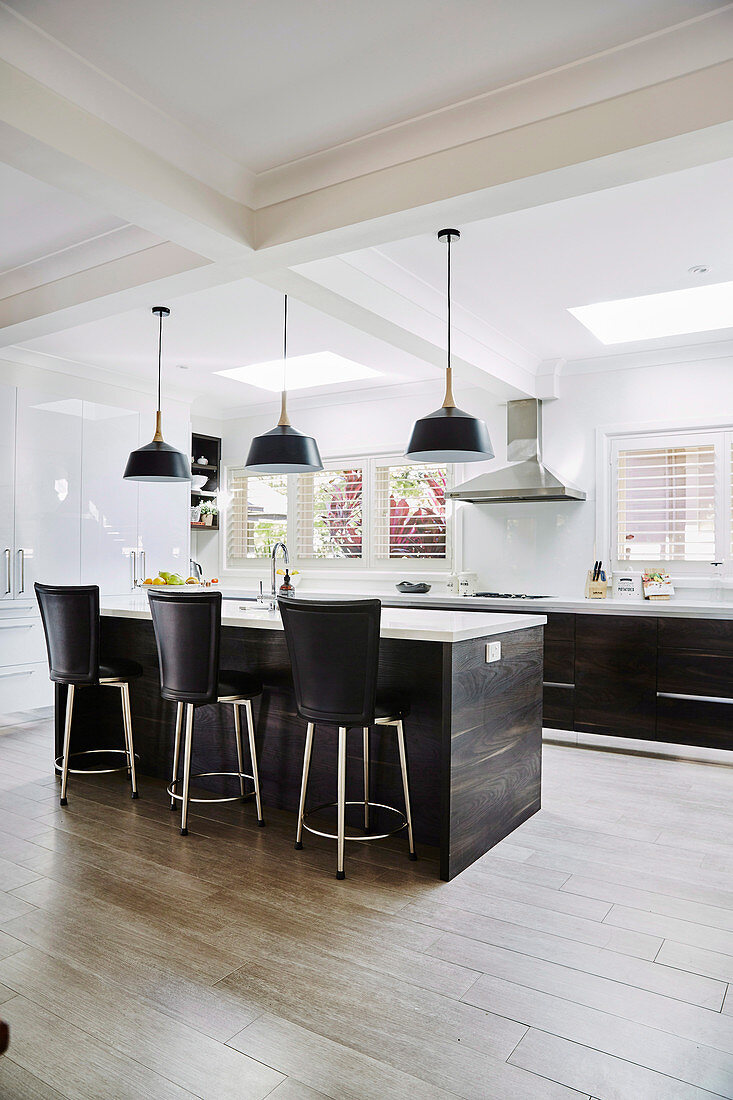 Middle block with bar stools in front of a kitchenette in an open kitchen with porcelain floor tiles in a wood look