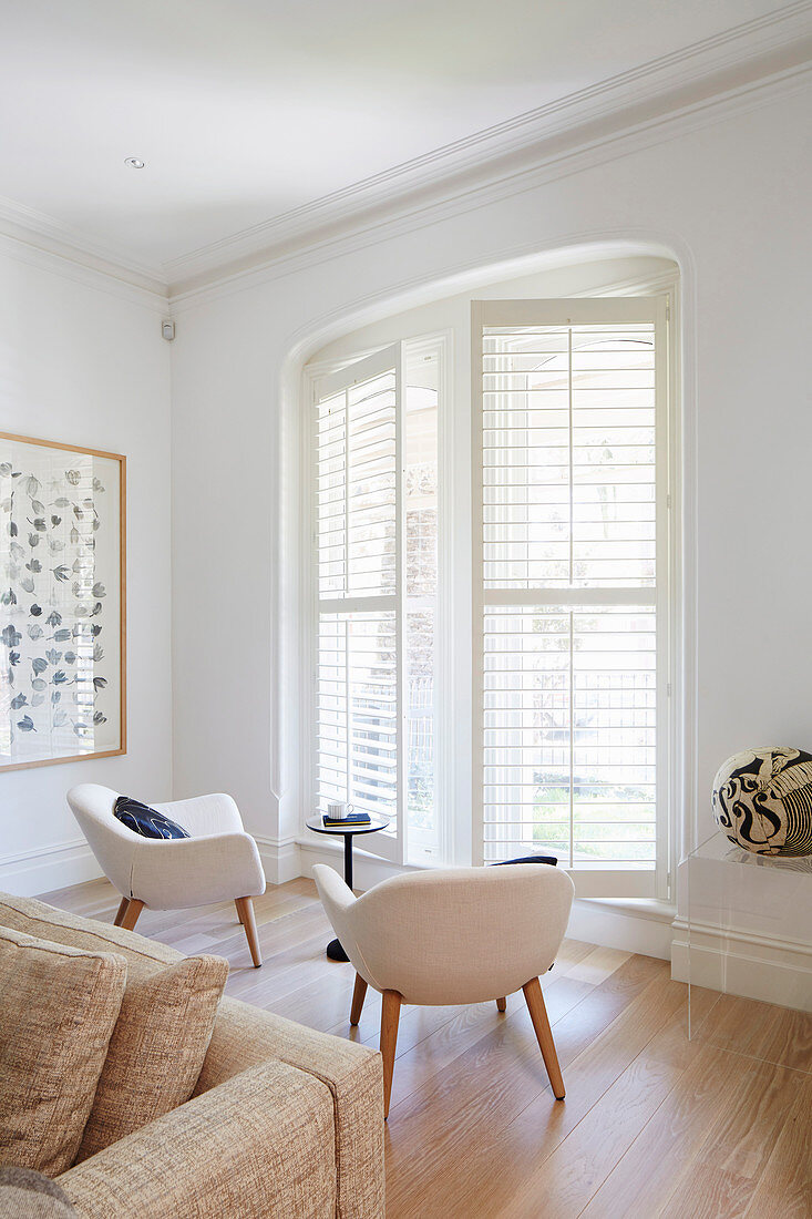 Two armchairs in the bright room in front, windows with shutters