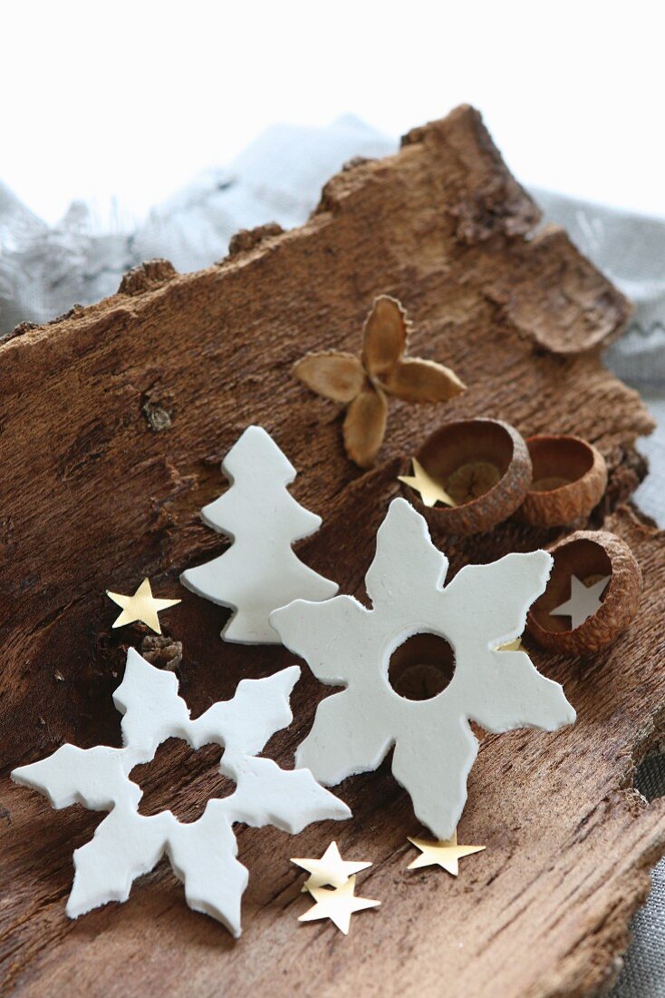Clay Christmas decorations in white and terracotta on piece of bark