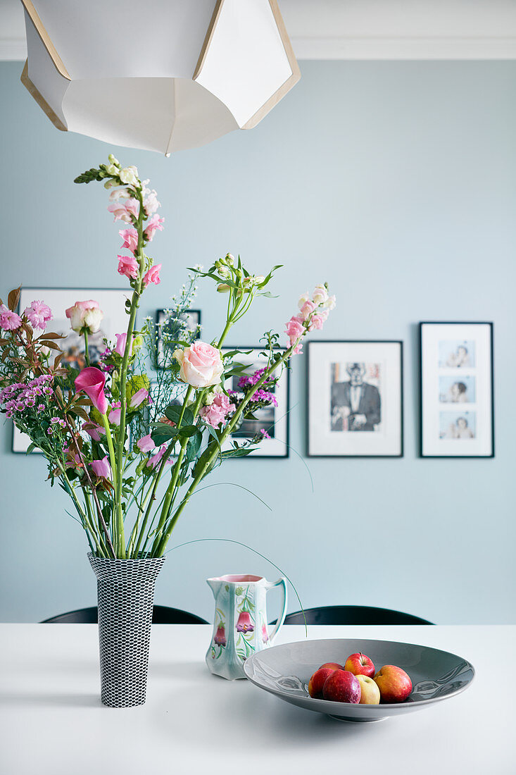 Blumenstrauß in Rosatönen auf dem Esstisch vor hellblauer Wand