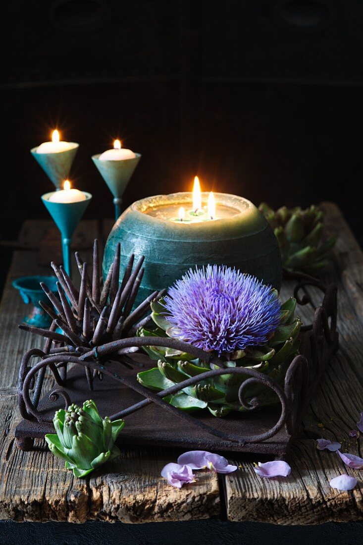 Artichoke flower and spherical candle on rusty metal tray