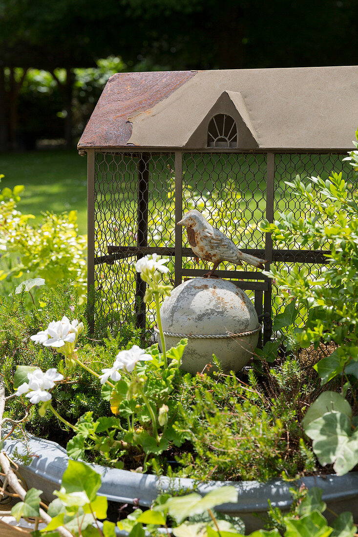 Vintage Vogelfigur vor Maschendraht-Käfig im Garten