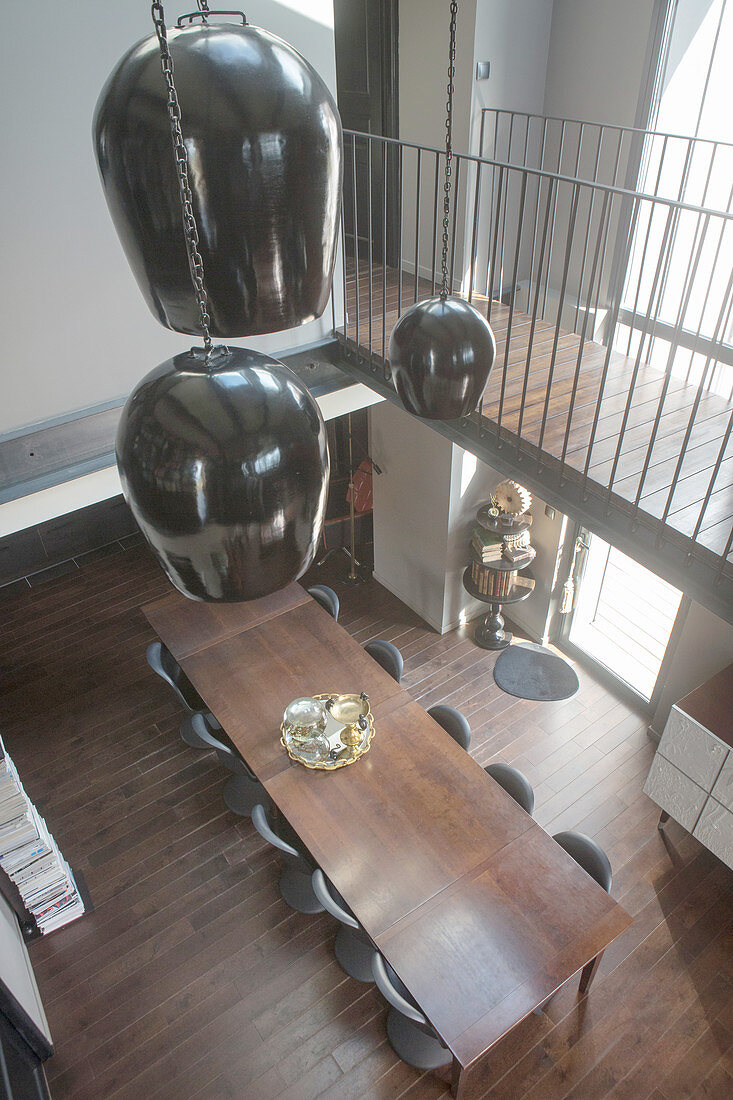 Schwarze Deckenleuchten hängen über dem Esstisch unter der Galerie