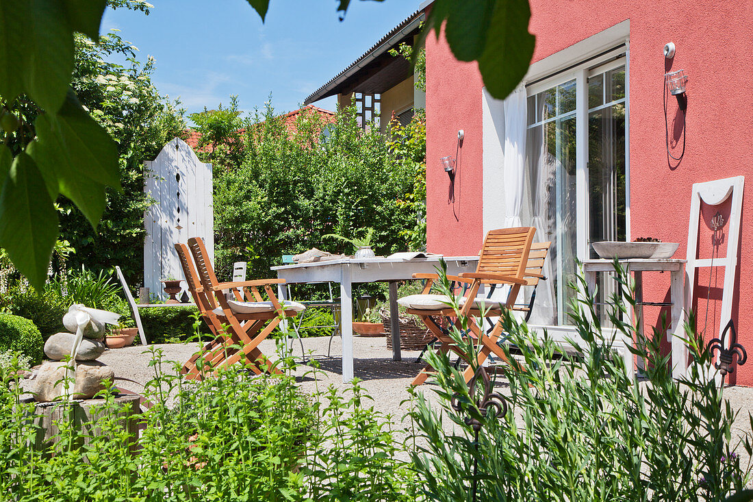 Tisch und Stühle auf der Terrasse im Garten vor einem roten Haus