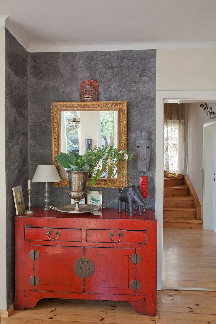 Red Oriental-style chest of drawers and ethnic accessories against grey wall