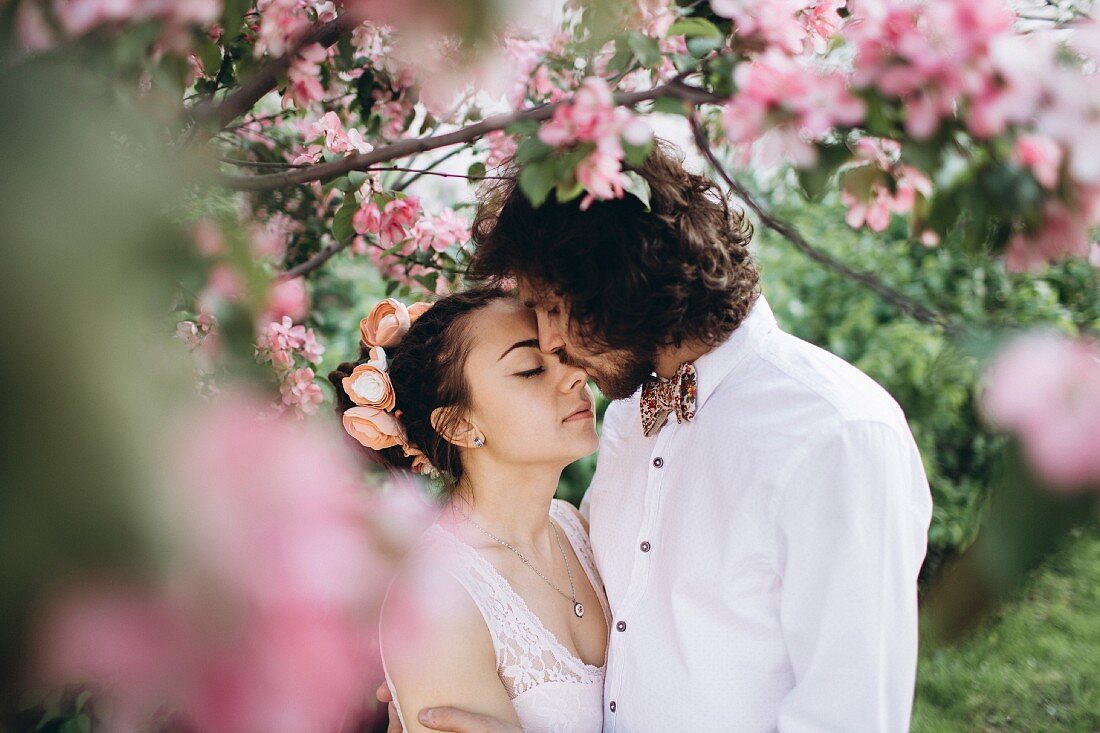 Bride and groom kissing under flowering tree