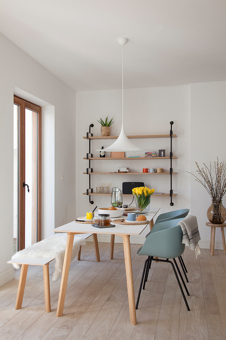 Dining table, shell chairs and bench next to balcony doors and in front of wall-mounted shelves
