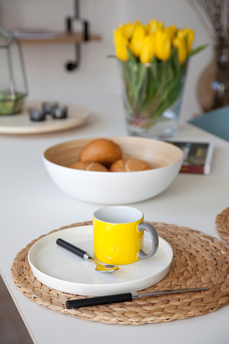 Teller mit gelber Tasse auf Korbuntersetzer auf Frühstückstisch