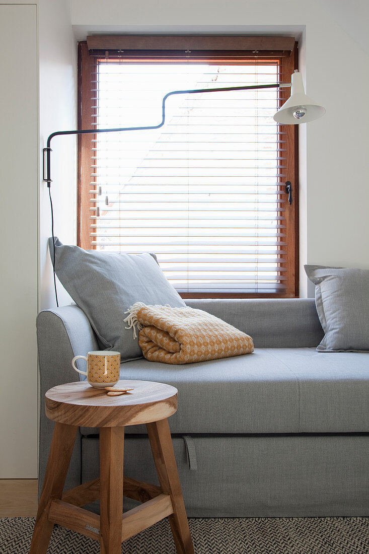 Wooden stool and grey sofa with scatter cushions in front of window