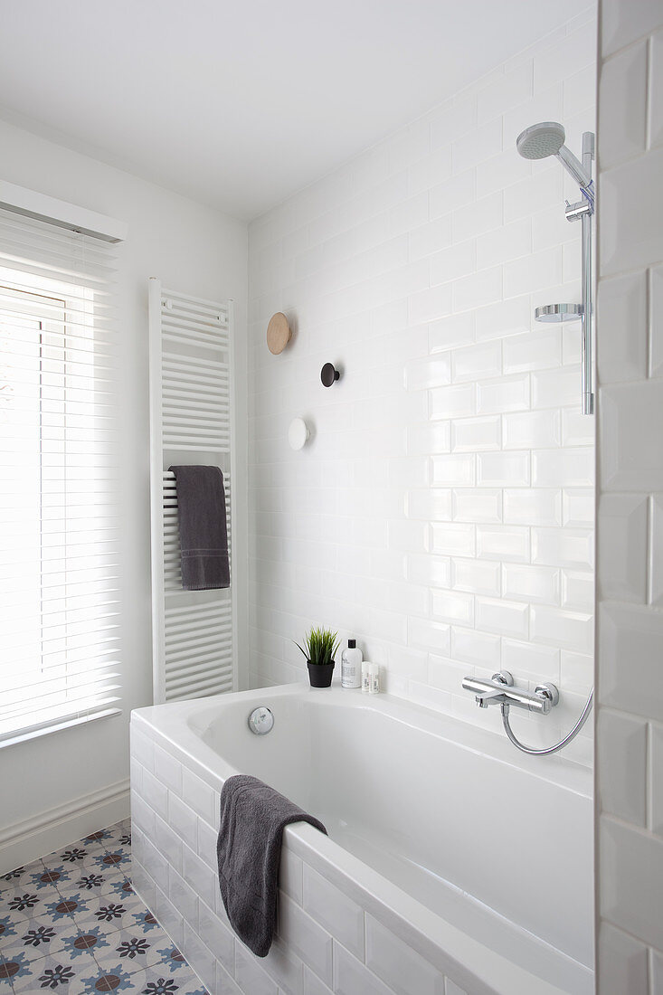 Bathtub, towel rail and window in white bathroom
