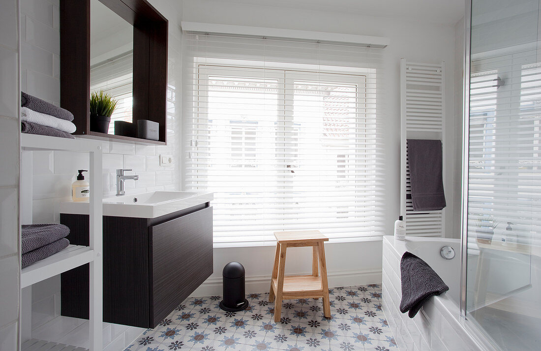 Sink, mirror, window with louvre blinds, towel rail and bathtub in bathroom