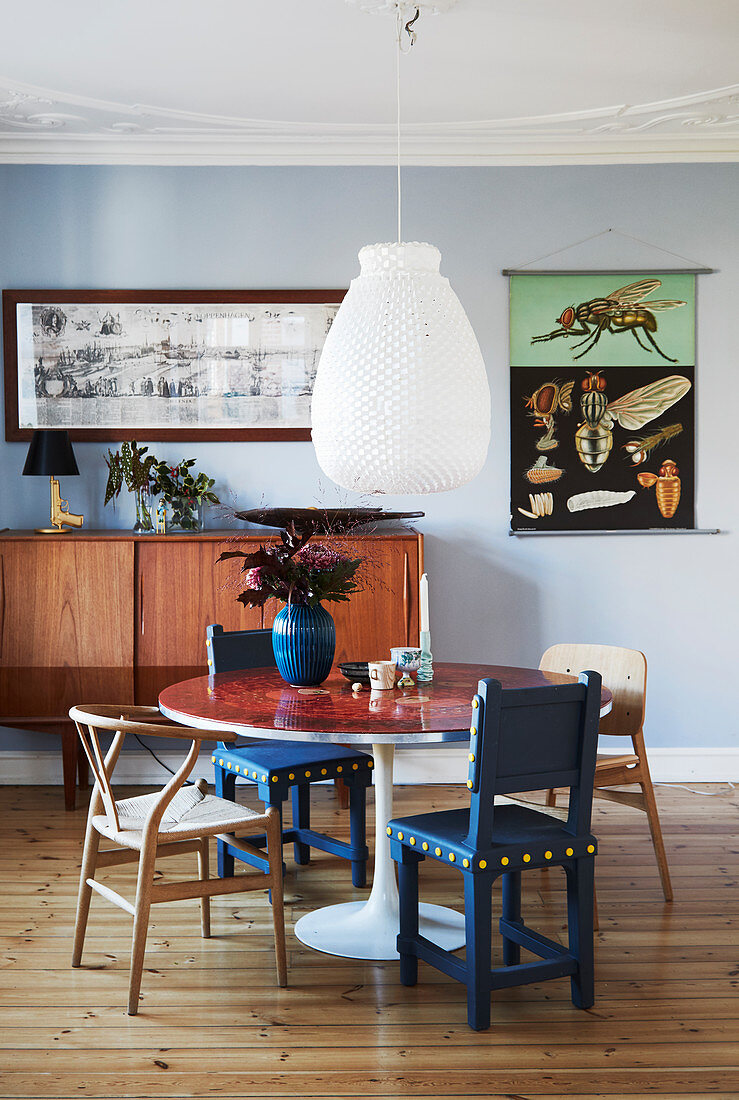 Verschiedene Stühle um einen runden Tisch vor blauer Wand