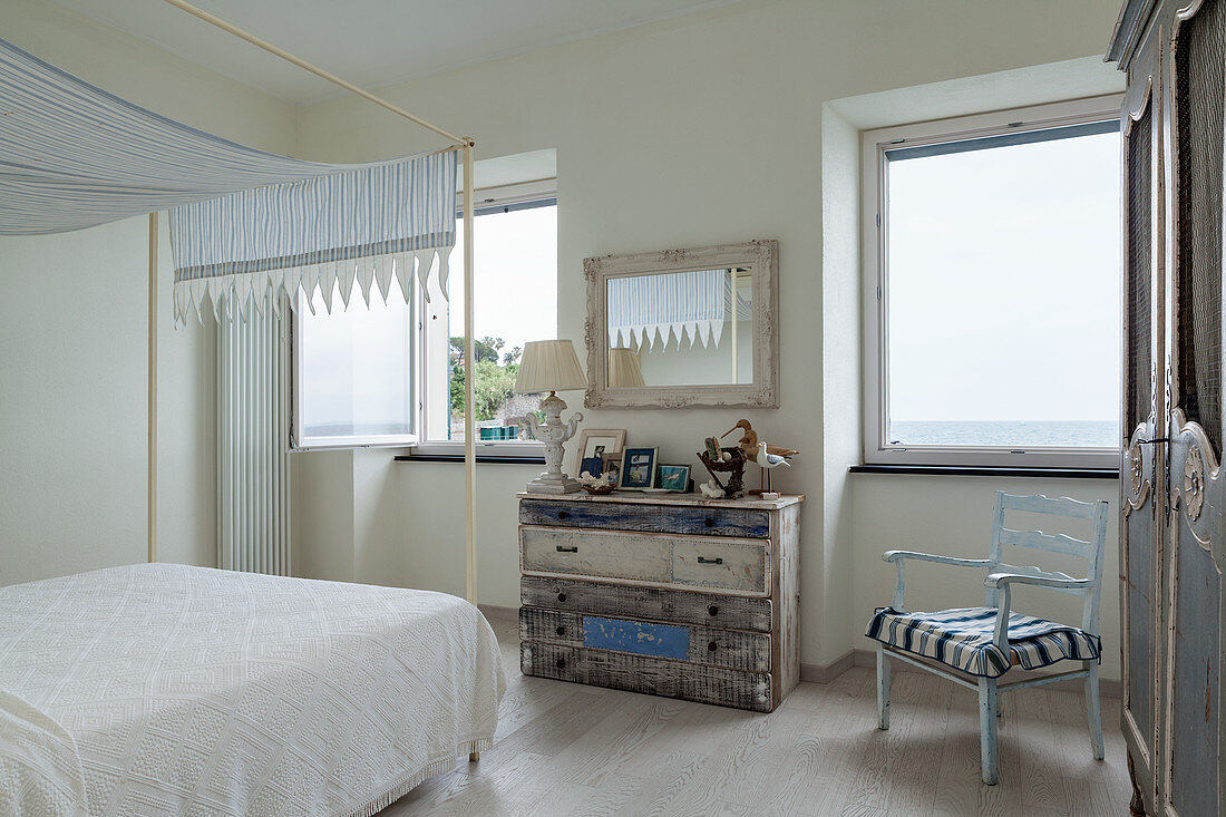 Shabby-chic chest of drawers in white and blue bedroom with sea view