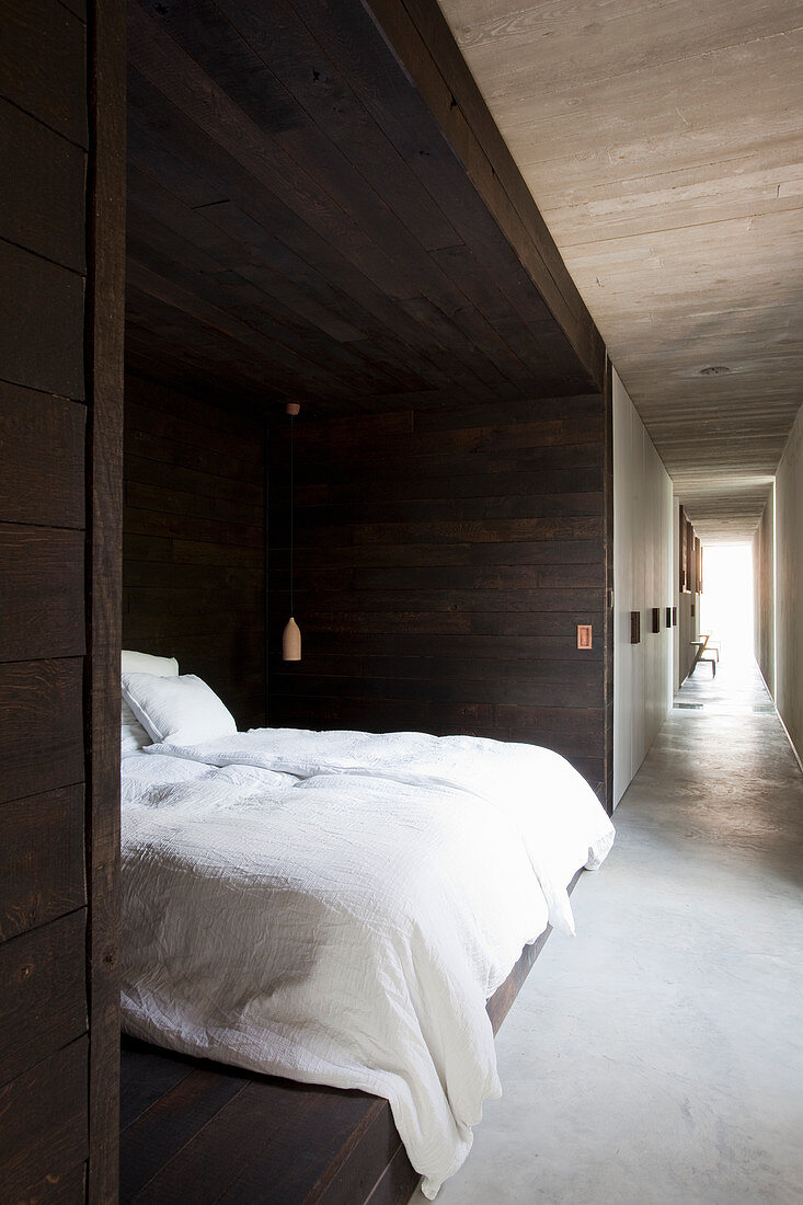 Bed in niche clad in dark wood and view along long corridor