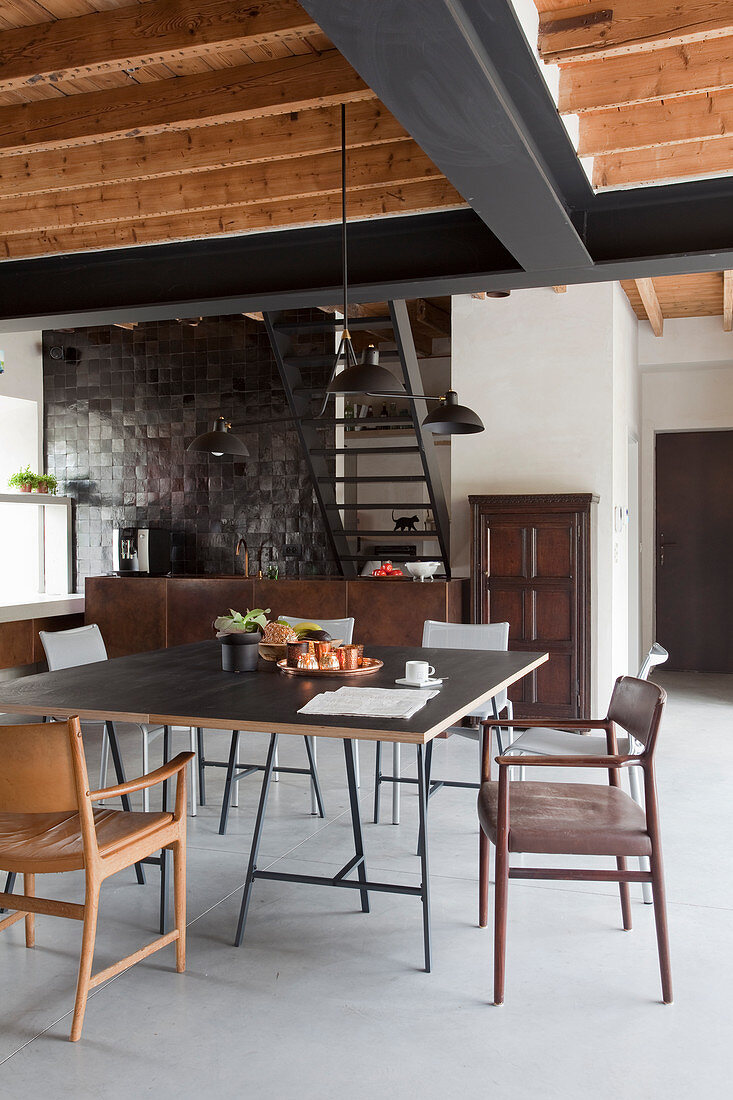 Various chairs around dining table in open-plan industrial-style kitchen