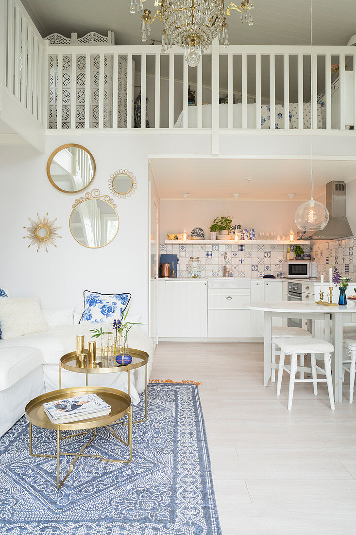 Offener Wohnraum mit weißer Couch, weißem Esstisch und Küche unter Galerie mit Schlafbereich