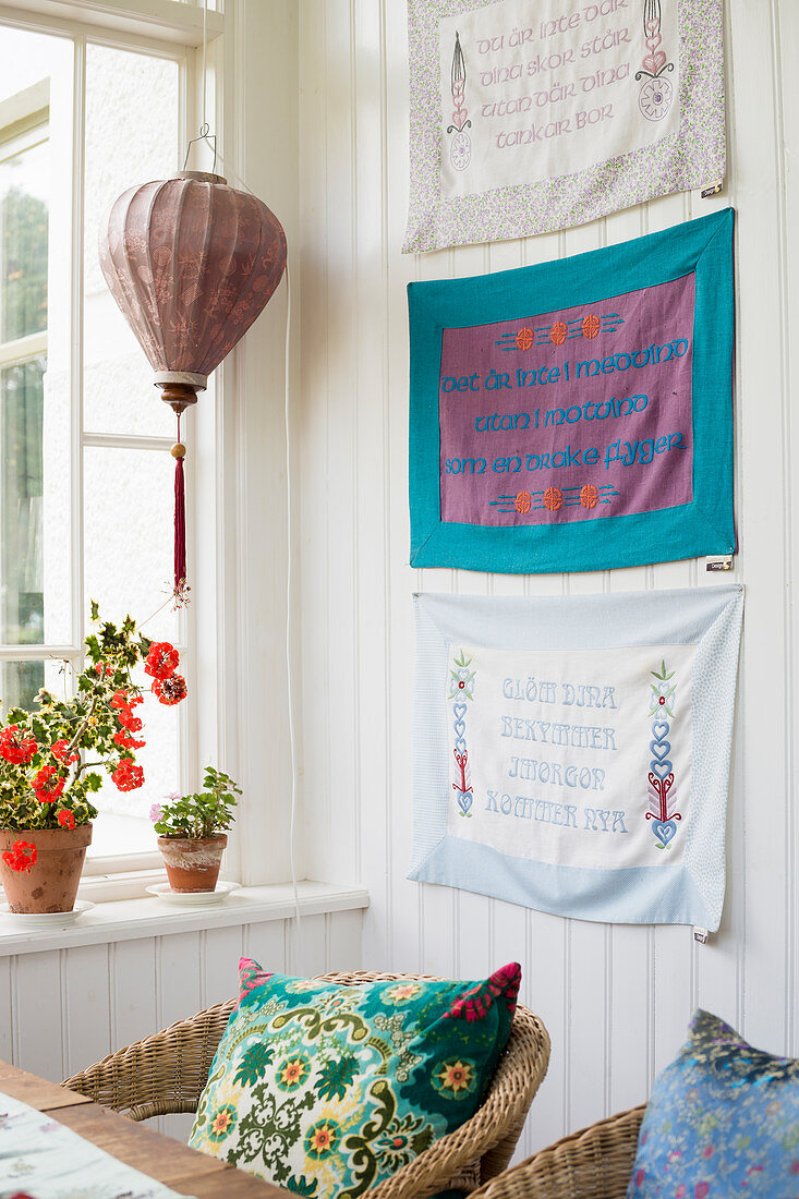 Wall hangings with lettering above rattan armchairs in conservatory