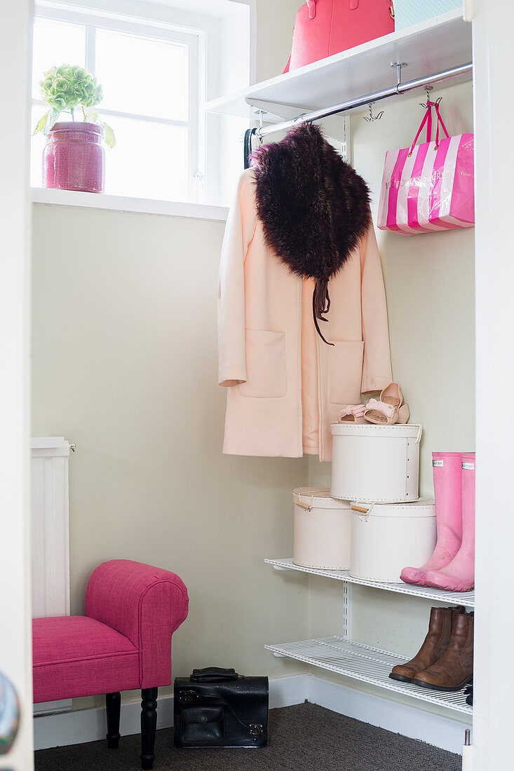 Woman's coat, hat box and pink accessories in white cloakroom