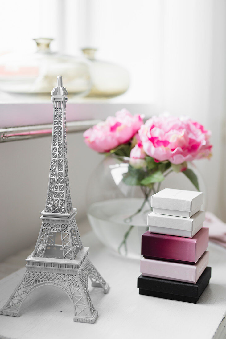Miniature Eiffel Tower, boxes and roses in spherical vase on bedside table