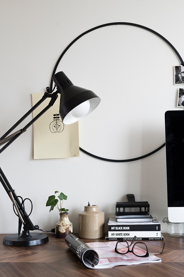 Black table lamp on desk and round black frame on wall used as pinboard