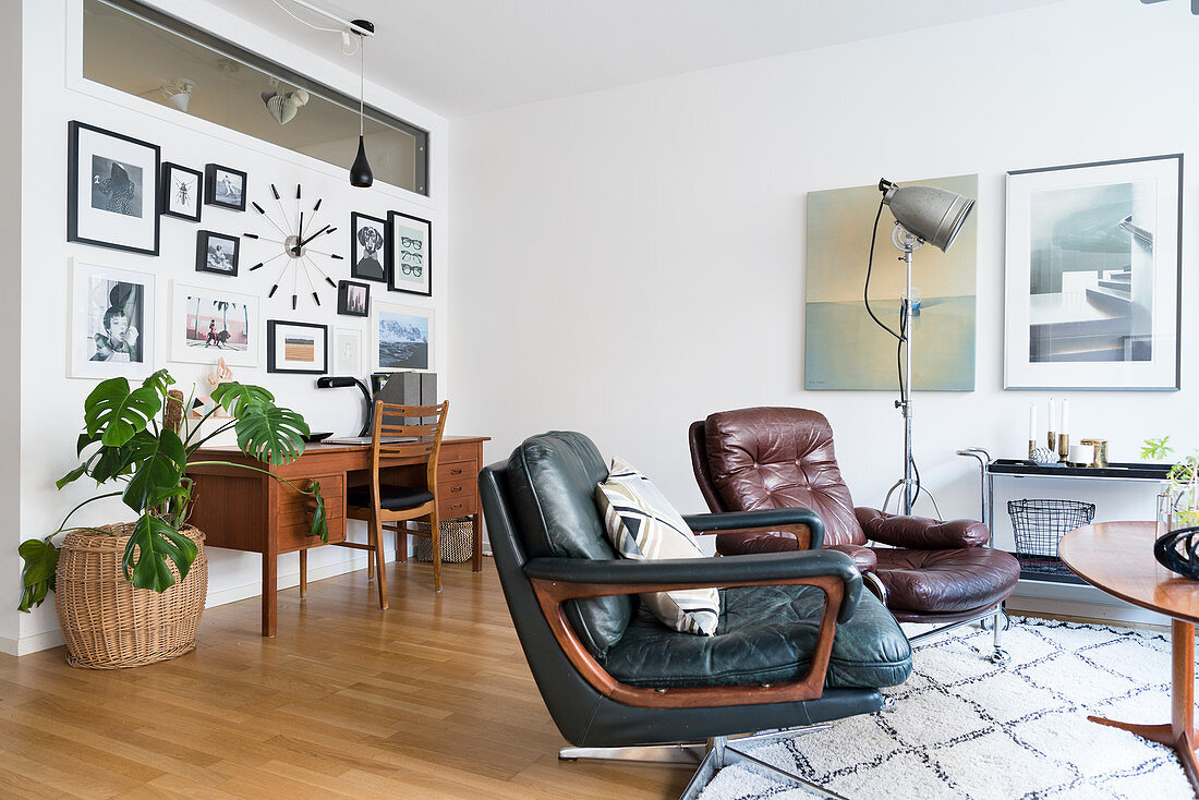 Two retro leather armchairs in front of desk below gallery of pictures on wall